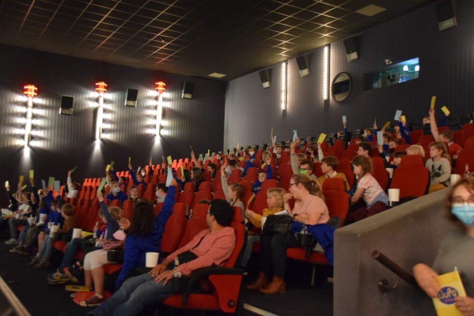 KiJuPaler*innen nehmen an einer Abstimmung zur 1. Konstituierenden Sitzung des 13. KiJuPas teil. Dazu halten Sie ihre Abstimmungszettel in die Höhe. Die Sitzung findet im Kinosaal des Cineplex statt.